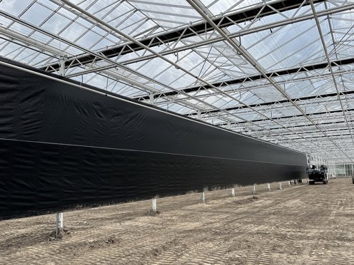zwart scherm halverwege een kas in aanbouw met losse grond en hoogwerkers 