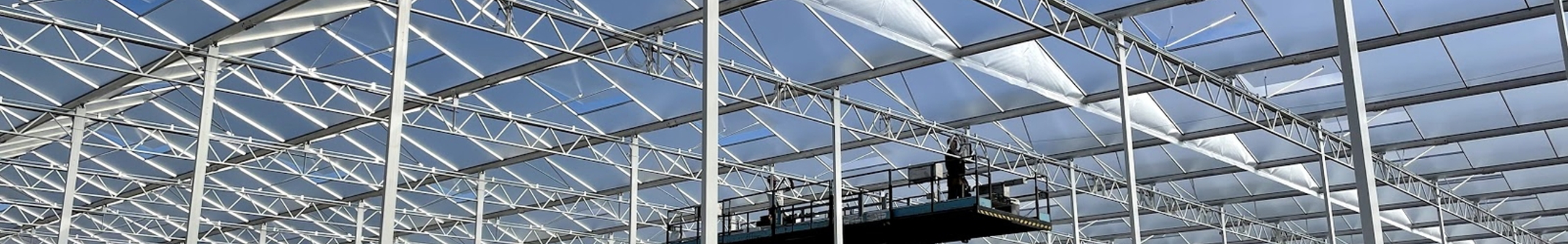 kas in aanbouw met hoogwerkers erin op de losse grond in de zon
