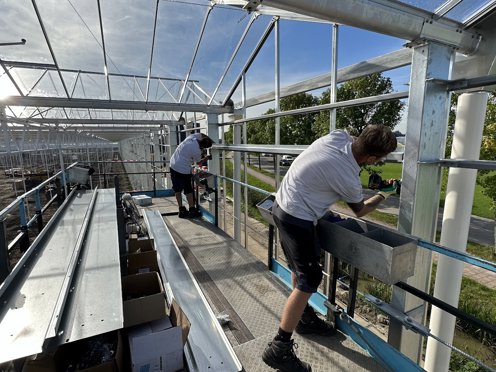 twee mannen op een hoogwerker in een kas aan het werk