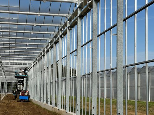 zijgevel van een tuinbouwkas in aanbouw met een hoogwerker met werkmannen erop