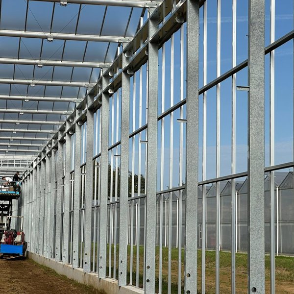 zijgevel van een tuinbouwkas in aanbouw met een hoogwerker met werkmannen erop