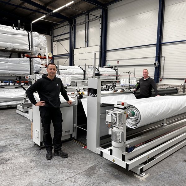 twee trotse mannen bij een confectiemachine in een bedrijfshal