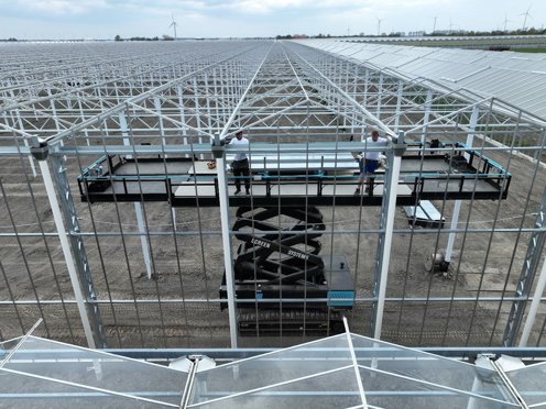 installateurs in witte shirt op hoogwerker in een kas in aanbouw