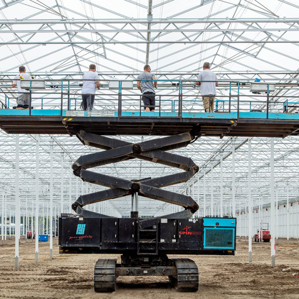 vijf mannen aan het werk op een hoogwerker in kas in aanbouw