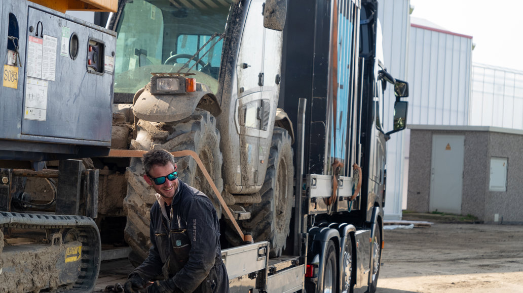 lachende man met zonnebril in vuile overall bij vrachtwagen die machines heeft opgeladen