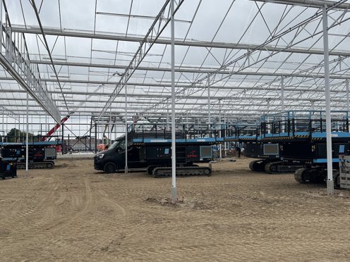 kas in aanbouw vol met hoogwerkers en hijskraan op de achtergrond