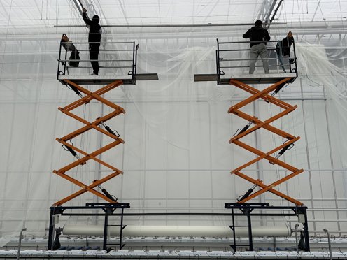 twee zwart oranje hoogwerkers met 2 mannen erop die met schermdoeken aan het werk zijn