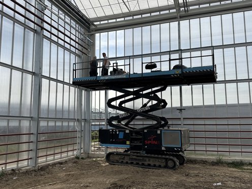 hoogwerker in kas in aanbouw met twee mannen aan het werk 