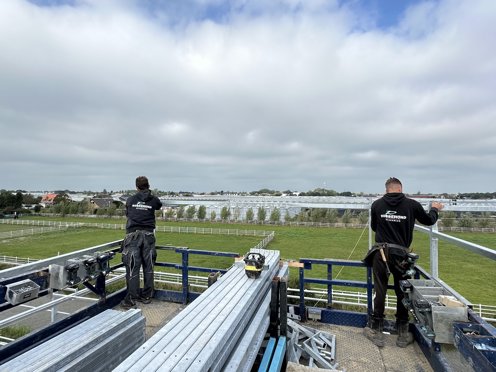 twee mannen werken aan stalen kasconstructie van een kas in aanbouw met vergezicht over weiland en kassen
