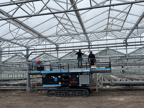 felblauwe hoogwerker met twee mannen aan het werk voor scherminstallatie in kas in aanbouw