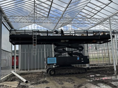aerial platform on boggy ground with man on it in greenhouse under construction