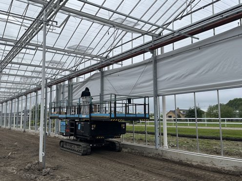 hoogwerker in kas in aanbouw bij een rolscherm