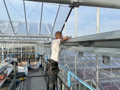 geconcentreerde jongeman op een hoogwerker in een kas aan het werk