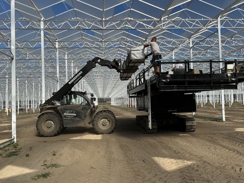 hoogwerker en shovel in een kas in aanbouw op een zonnige dag