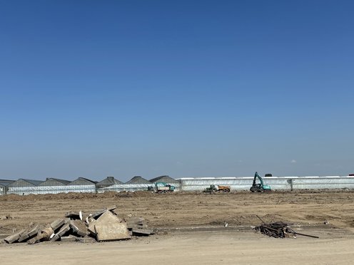 strakblauwe lucht en op voorgrond zandvlakte die klaargemaakt wordt voor kassenbouw met machines in de verte