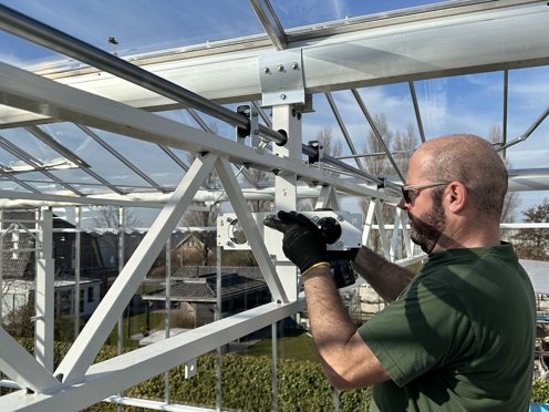 Man install screen cloths in a horticultural greenhouse on a sunny day