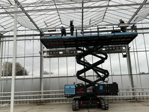mannen op hoogwerker installeren schermdoeken in kas in aanbouw