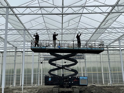 drie mannen in een kas op een hoogwerker installeren schermdoeken