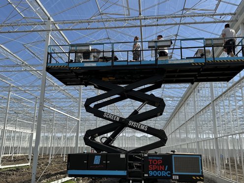 hoogwerker met mensen in een kas tussen de stalen constructie