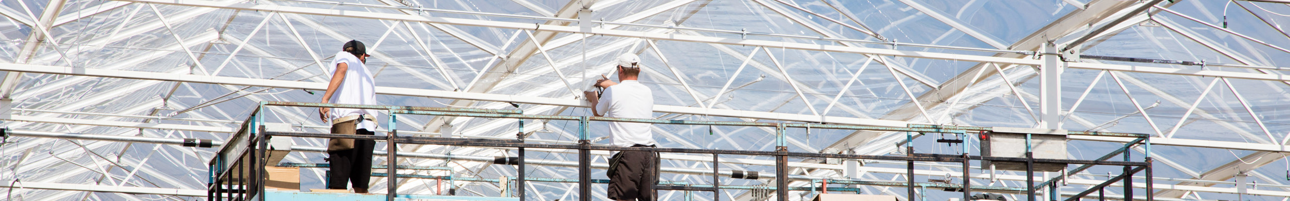 twee mannen op hoogwerker installeren in kas horizontale schermen 