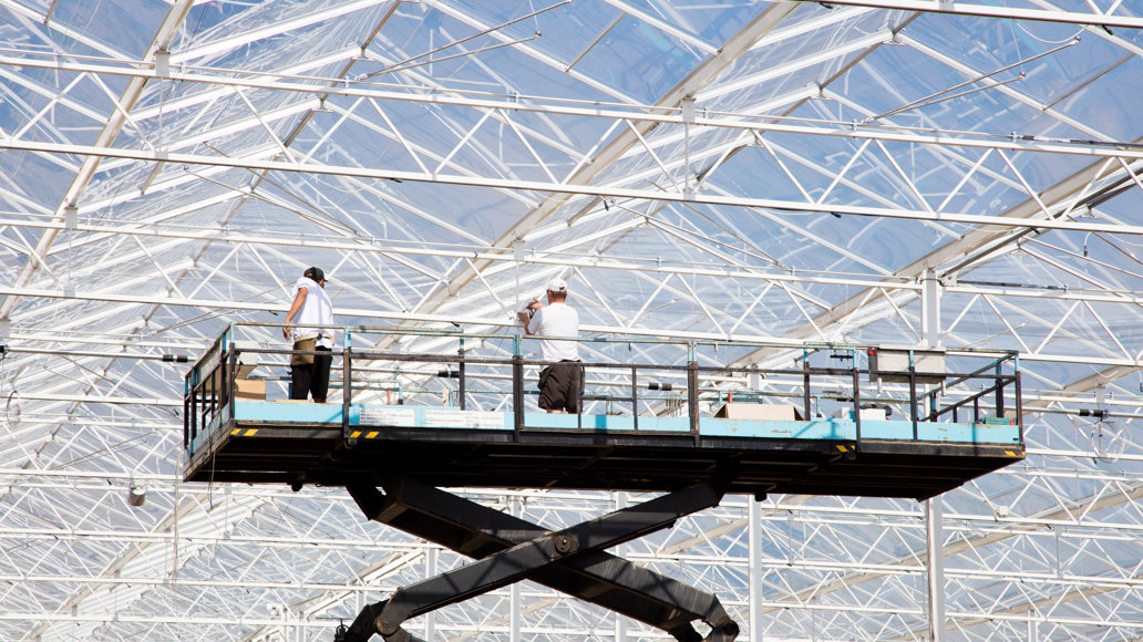 twee mannen op hoogwerker installeren in kas horizontale schermen 