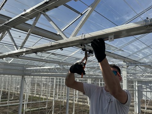 man installeert schermdoeken in de zon in de nok van een kas in aanbouw